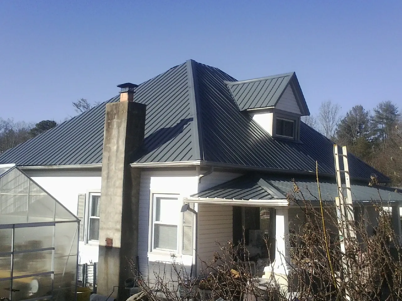 Dark blue standing seam metal roof on a white farmhouse with dormer — Slate & Tile Roof Repair by Roofing Brothers in Clarkrange
