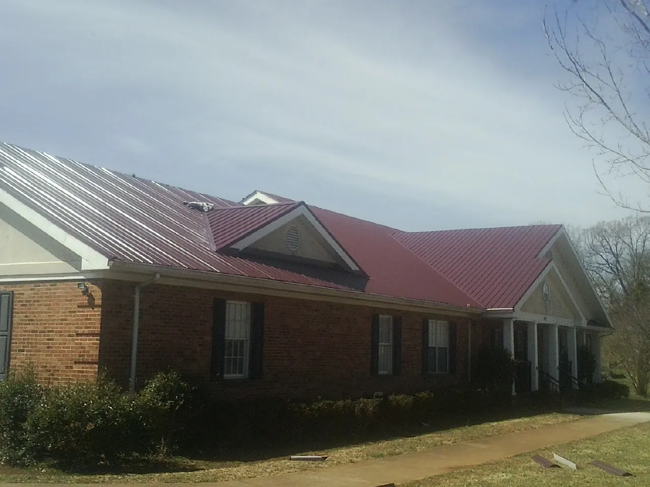 Red metal roof with gabled entries on a long brick building, from a Hail Damage Roof Repair job in Clarkrange