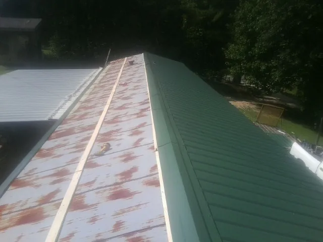 Old rusted panels beside newly installed green metal roofing — Wind Damage Roof Repair by Roofing Brothers in Clarkrange