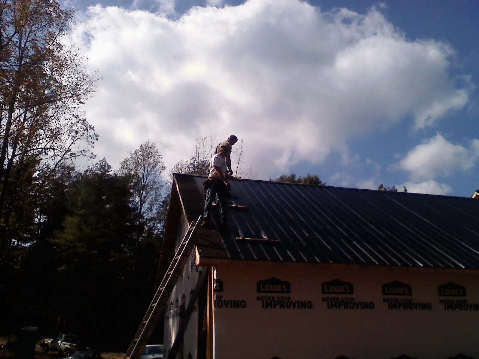 Roofer fastening dark metal panels high against a cloudy sky, from a Roof Inspection job in Clarkrange