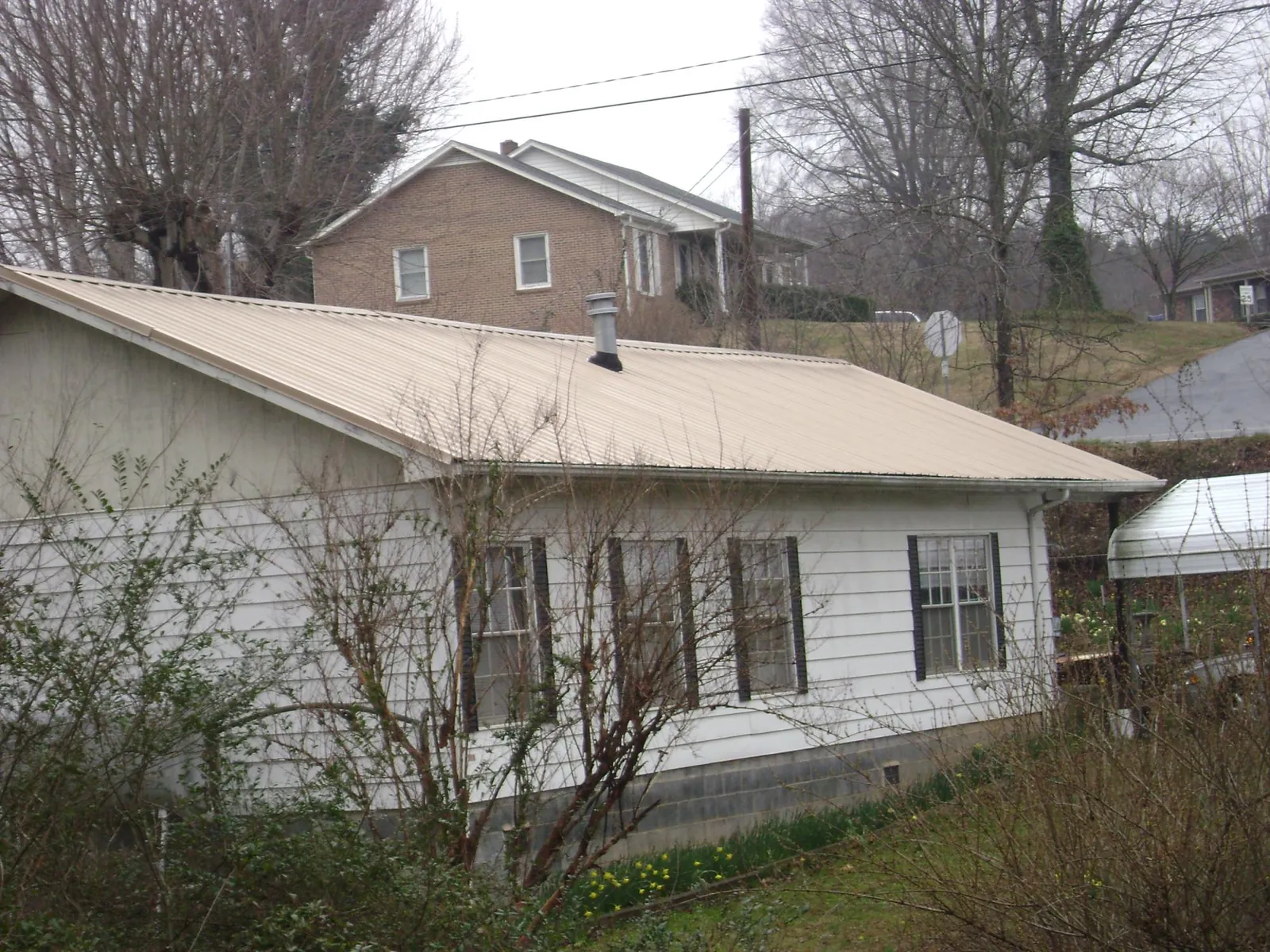 Tan metal roof on a white sided house set into a hillside — Commercial Roofing by Roofing Brothers in Clarkrange